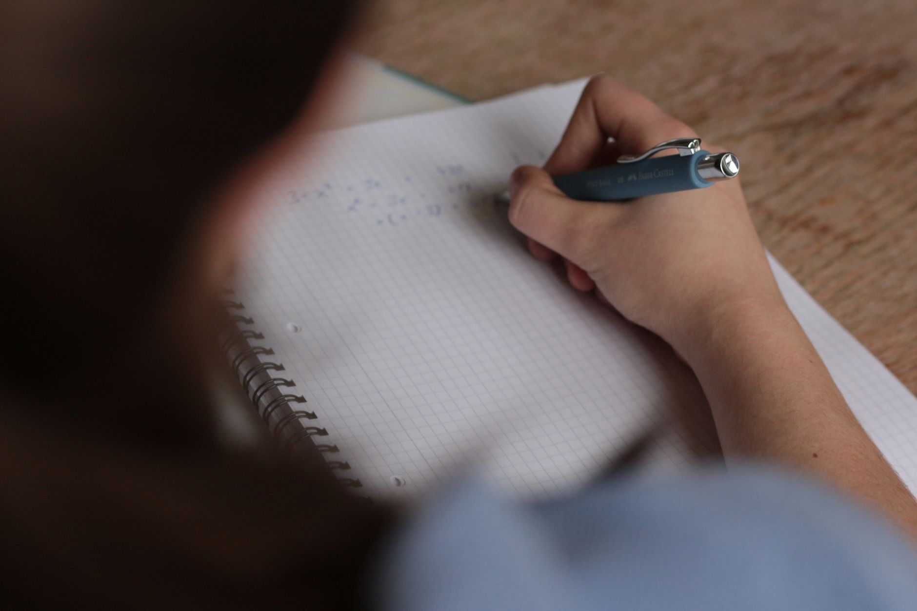 Iemand maakt met een pen aantekeningen in een notitieboek, gefocust op studeren.